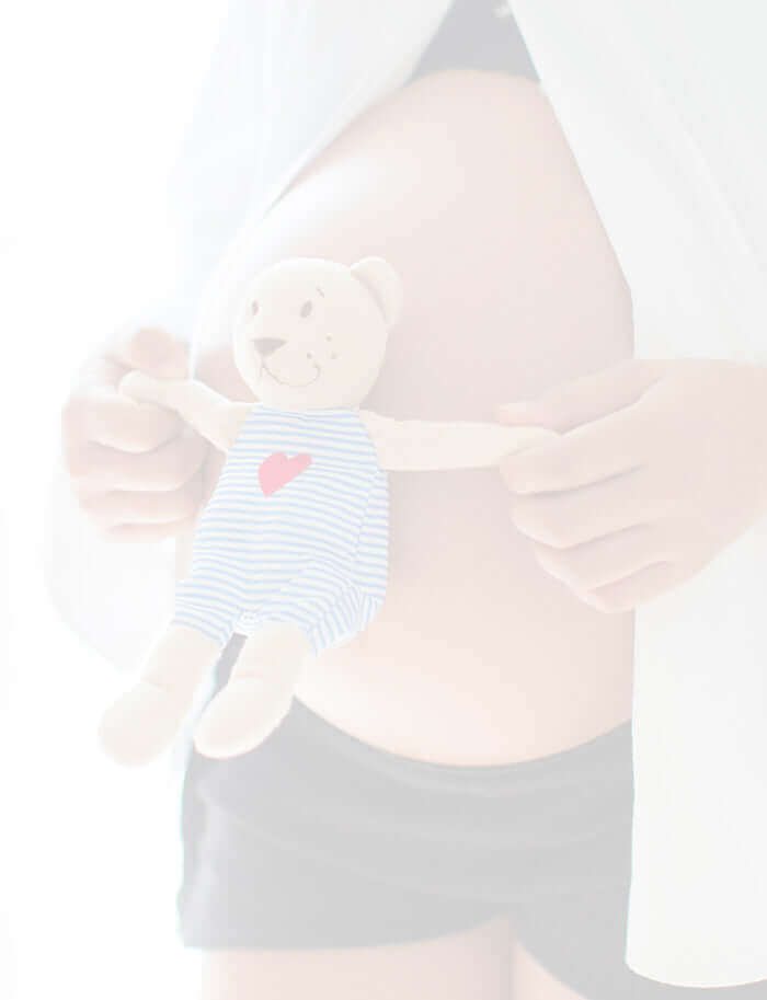 Pregnant lady holding a small cute teddy against her bump