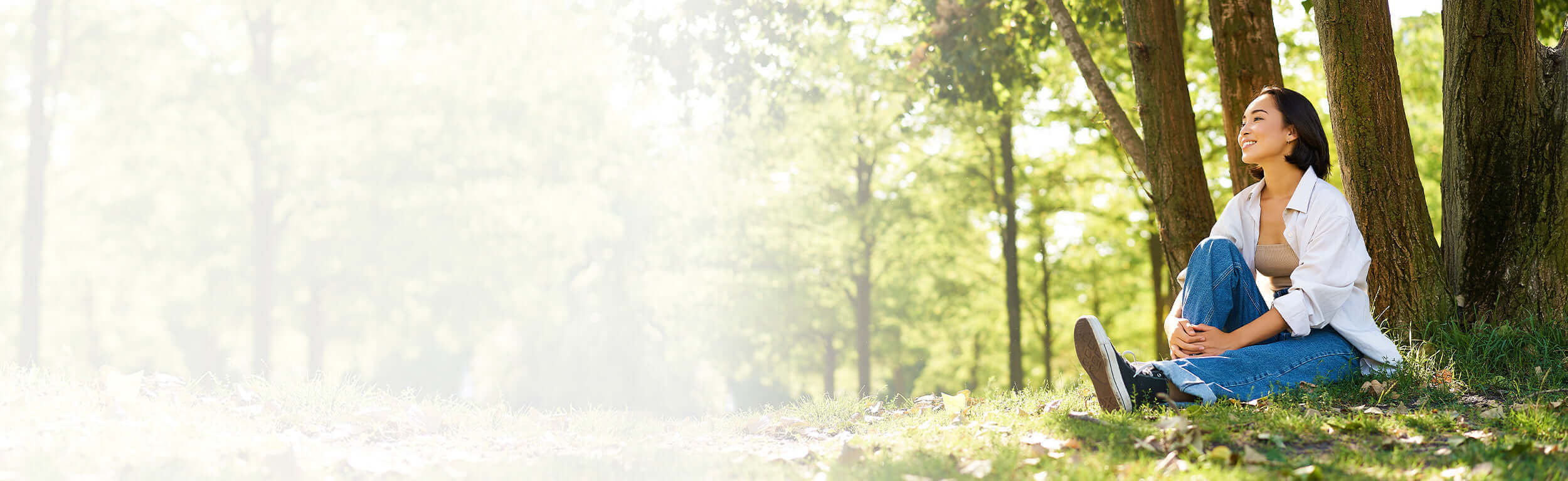 A woman sitting and leaning against a tree in the woods