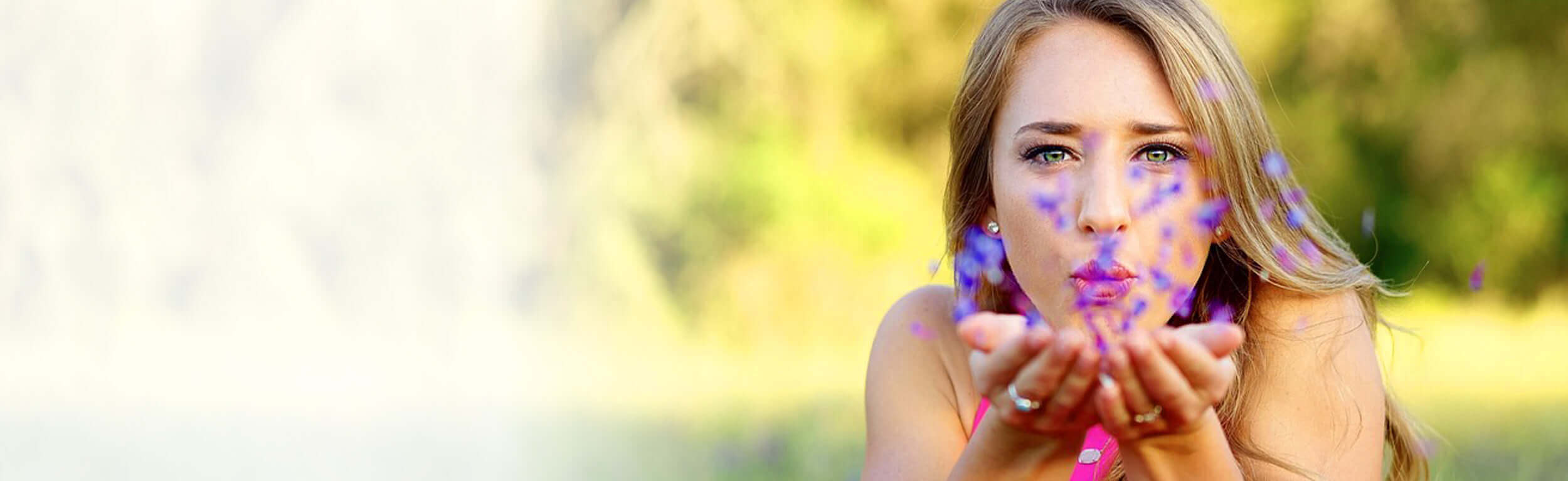 A woman blowing purple flower petals at the camera