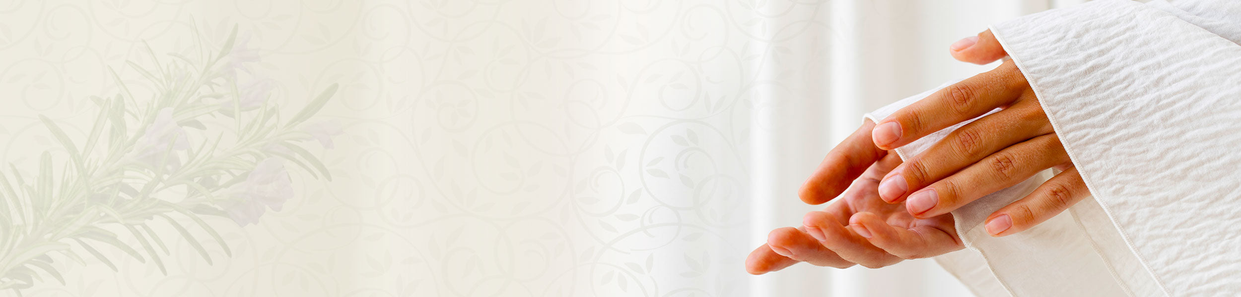 Close-up of hands applying oil in a white robe with a soft floral background.