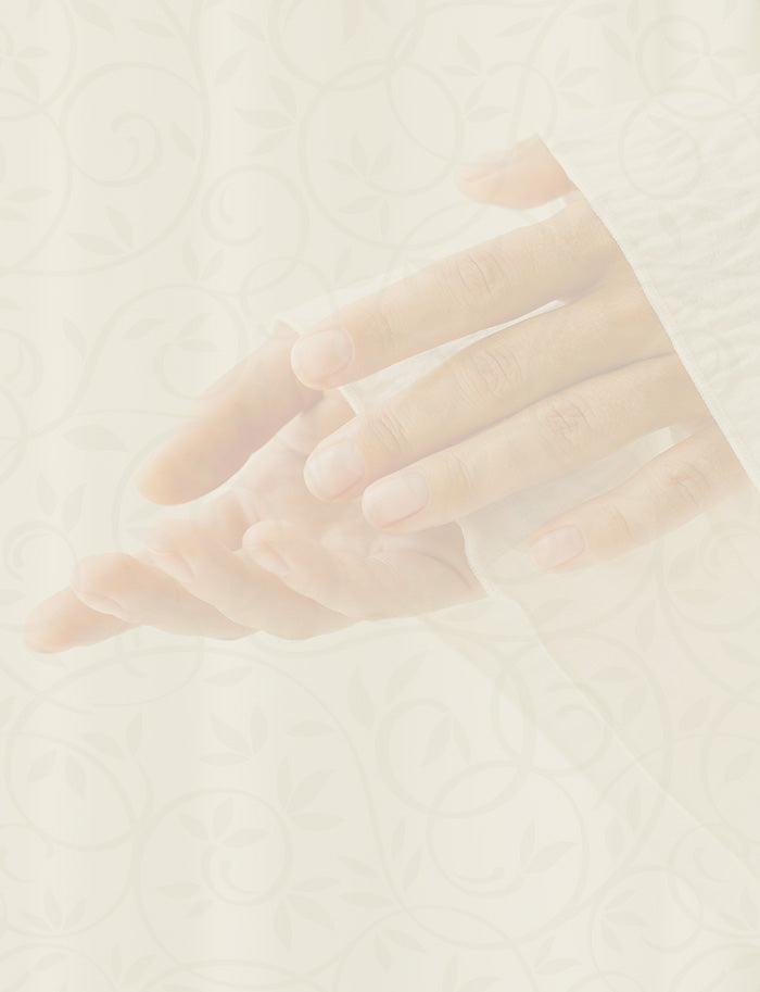 Hands applying oil while wearing a white robe, set against a light floral background