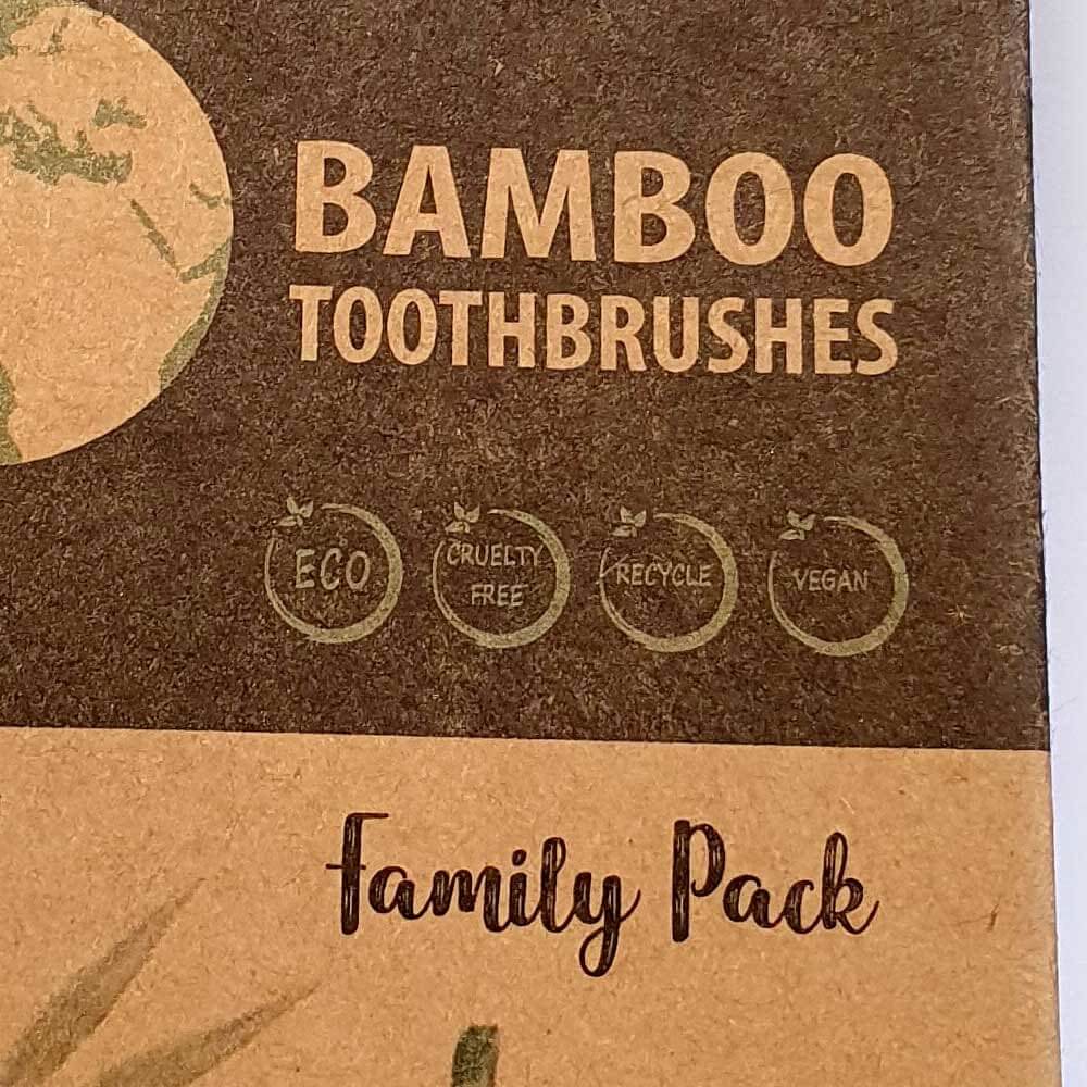 Close-up of bamboo toothbrush packaging showing ‘Bamboo Toothbrushes Family Pack’ with eco, cruelty-free, recyclable, and vegan icons on natural brown cardboard.