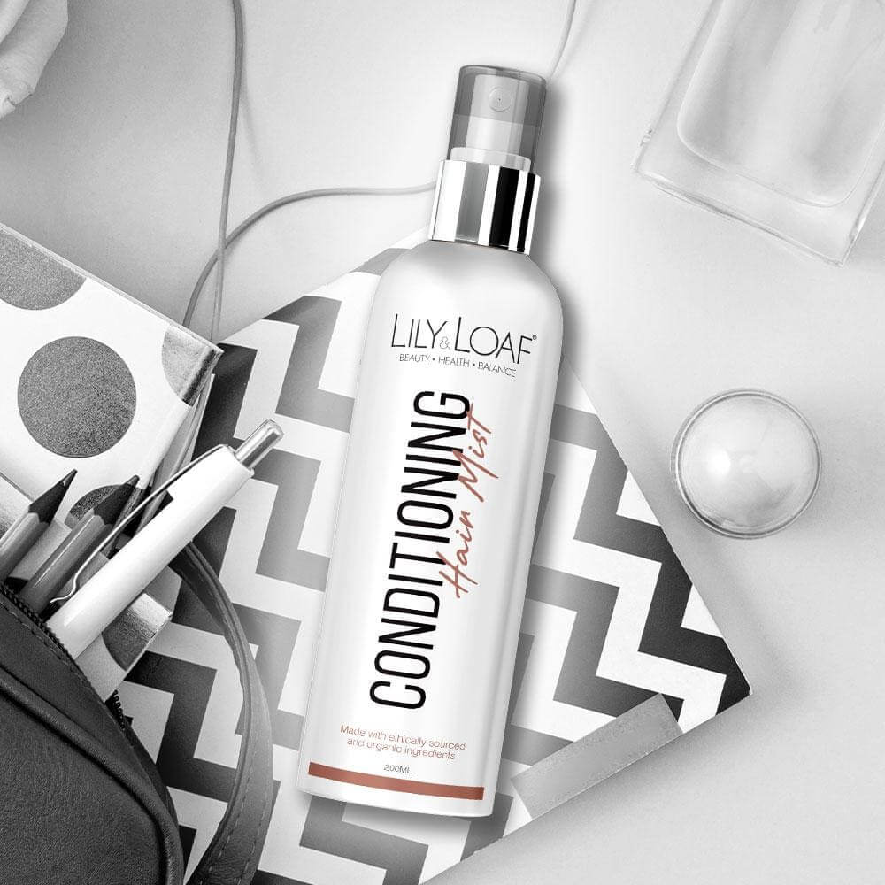 Lily & Loaf Conditioning Hair Mist on a chevron notebook with pens, a pouch, and beauty accessories