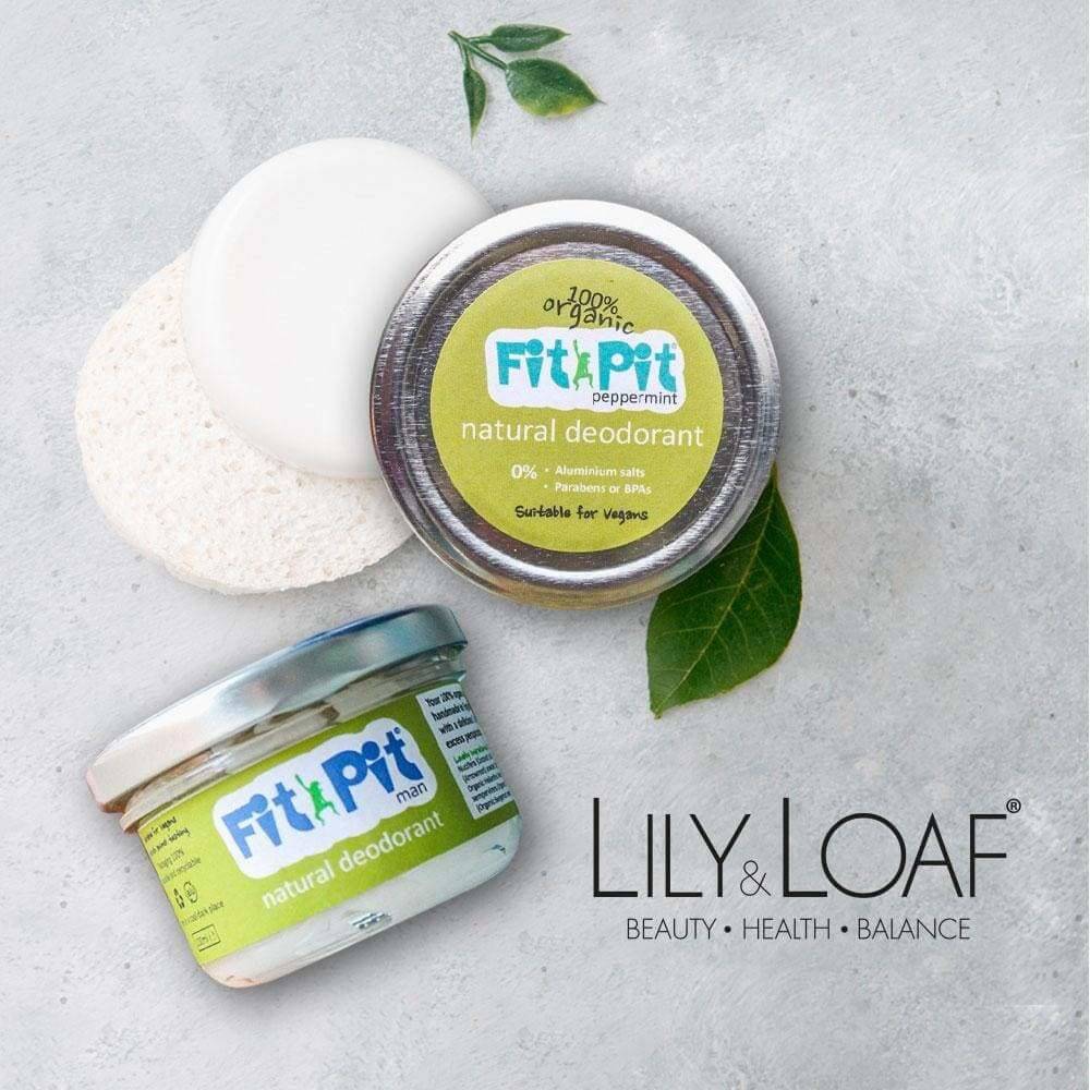 Two jars of Lily & Loaf Fit Pit natural deodorant on grey surface with green leaves. One tin is peppermint, the other Fit Pit man. Lily & Loaf logo at bottom right