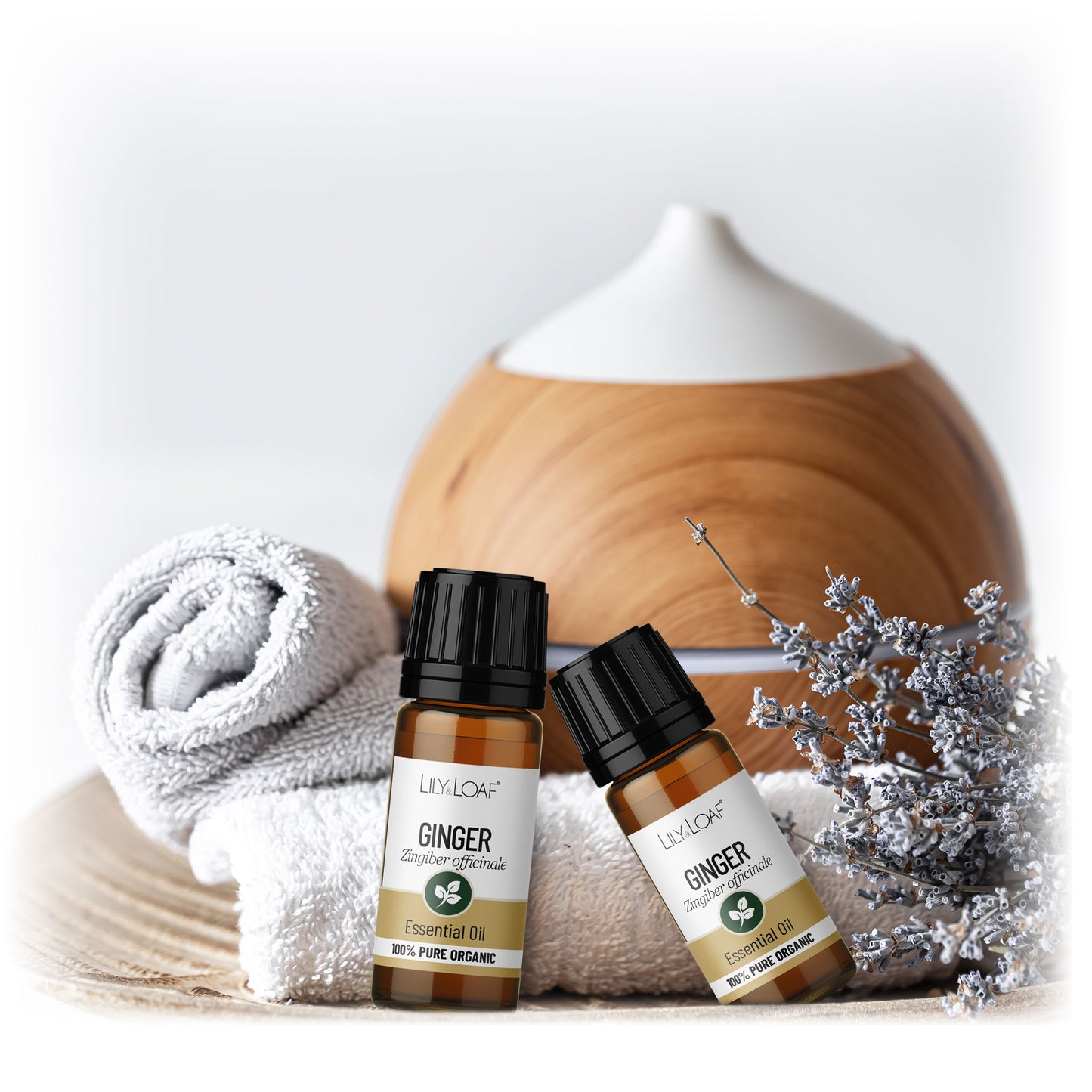 Two Lily & Loaf Ginger Organic Essential Oil bottles with diffuser, towels and dried lavender for a relaxing aromatherapy setup