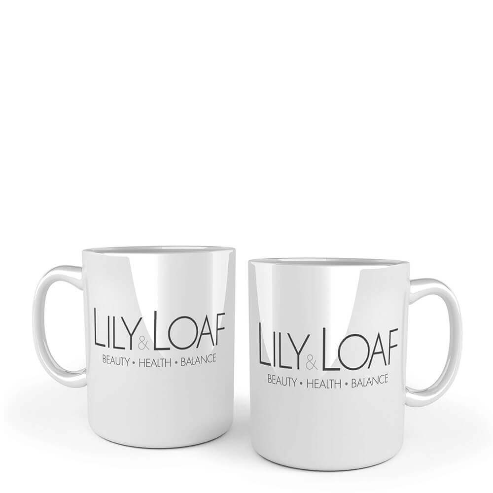 Two white ceramic mugs with handles, each printed with the Lily & Loaf logo and the tagline 'Beauty • Health • Balance', set against a plain white background.