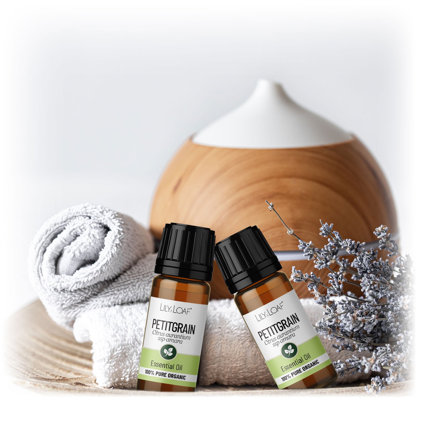 Lily & Loaf Petitgrain essential oil bottles with towel, diffuser, and lavender on wooden surface for aromatherapy.