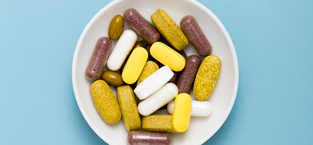 A bowl of assorted colourful supplements, including capsules and tablets, on a light blue background