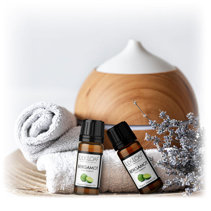 Lily & Loaf Organic Bergamot Essential Oil bottles with a diffuser, rolled towel, and dried flowers, creating a calming and aromatic spa-like setting.