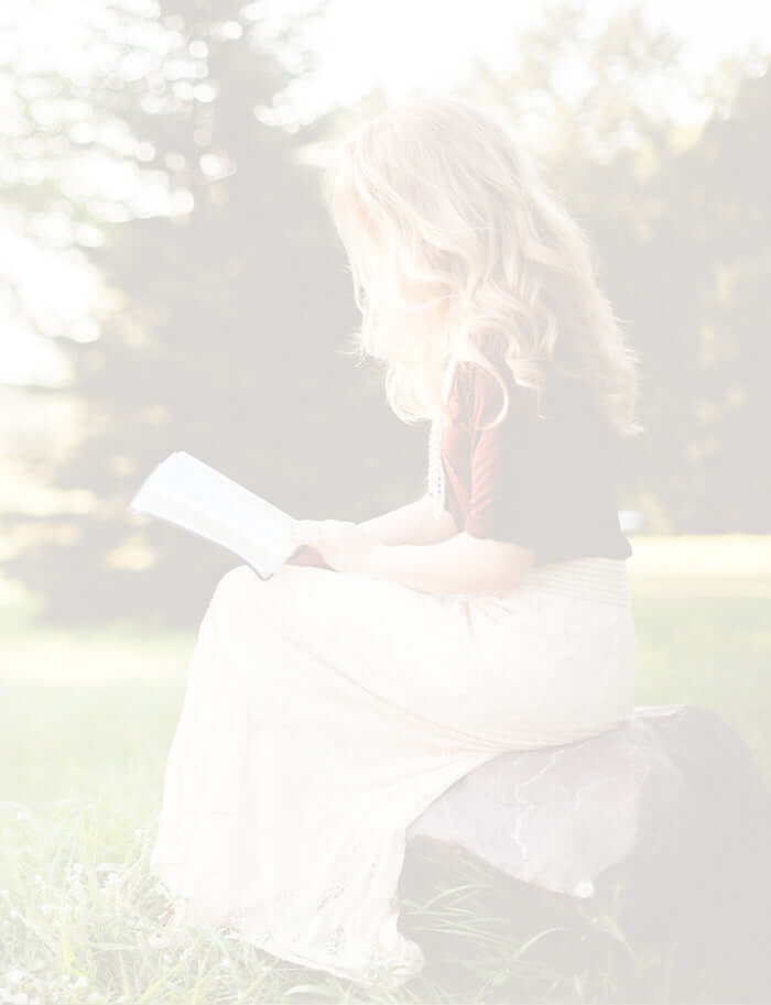 Lady sitting on a rock in a meadow, reading a book