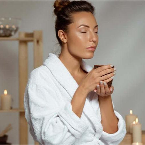 A woman in a white spa robe smelling a fragranced candle