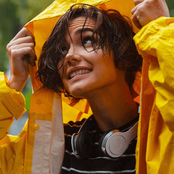A woman in a yellow raincoat holding her hood up to escape a rainstorm.