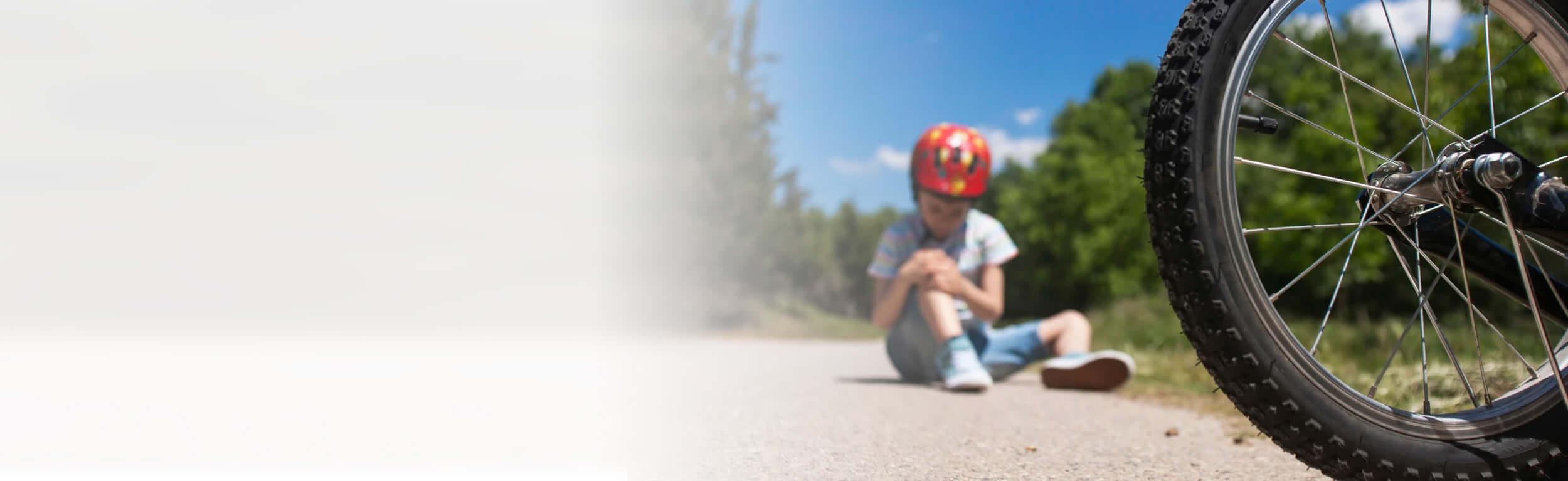 A boy in a red helmet looking at his knee after falling from his bike